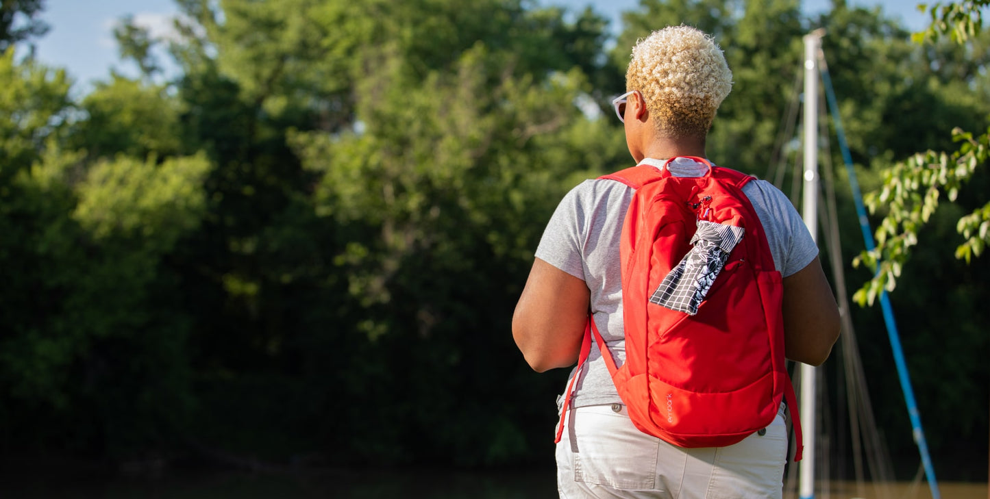 A person wearing a backpack with a pStyle in a pCase clipped to it. 