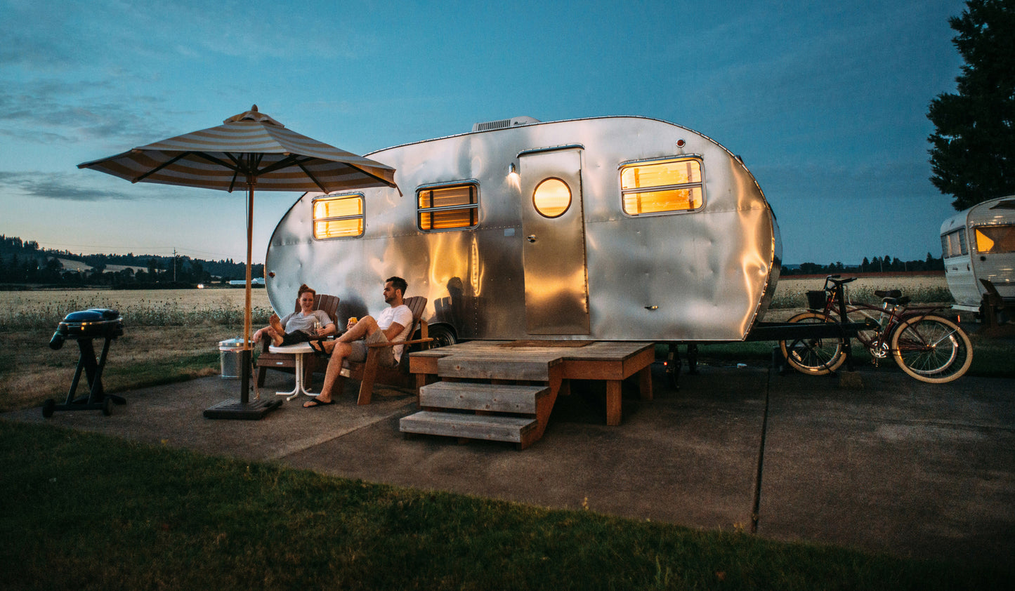 Two people hanging out next to an RV-style trailer. 