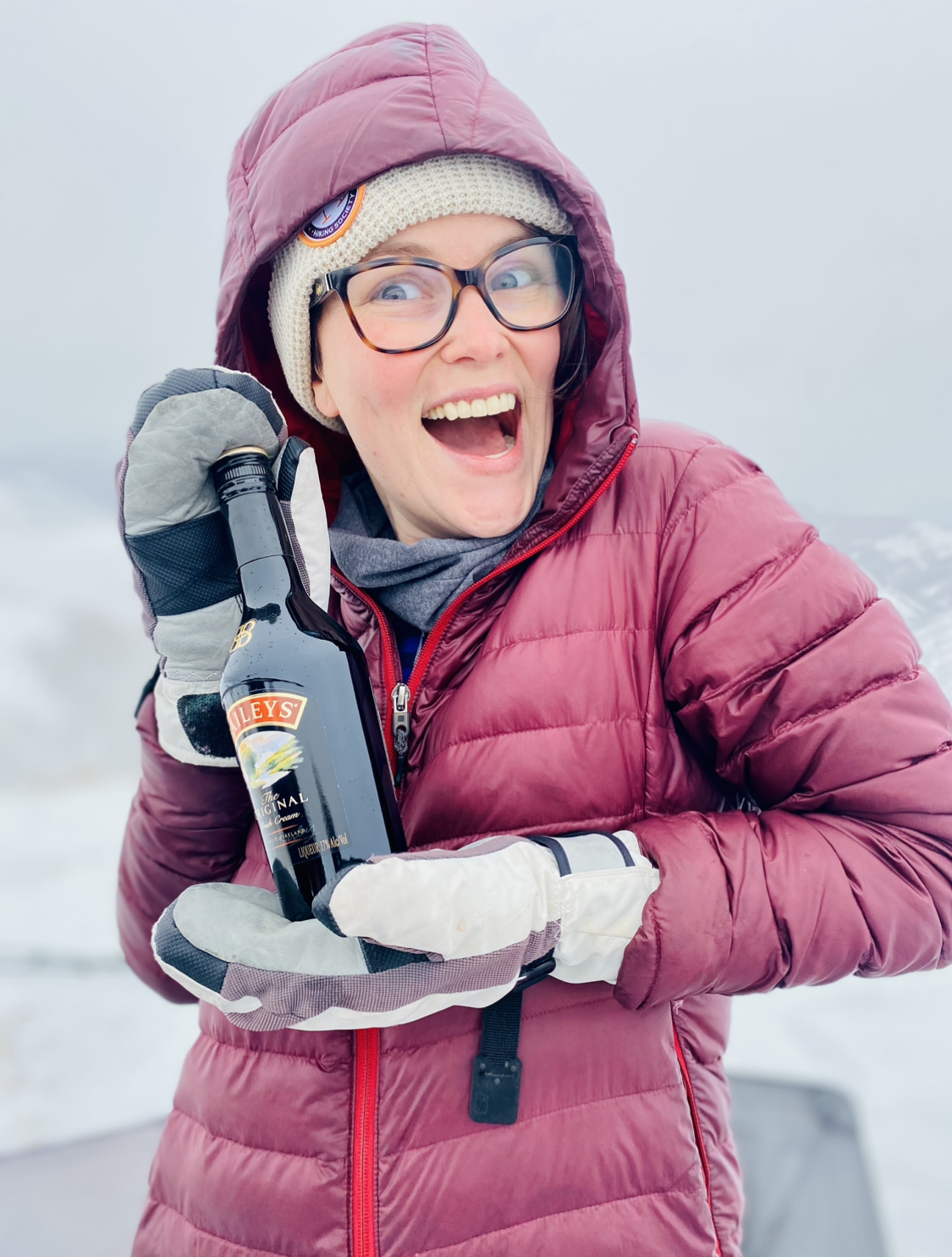 A woman in winter clothes holding a bottle of liquor and laughing. 